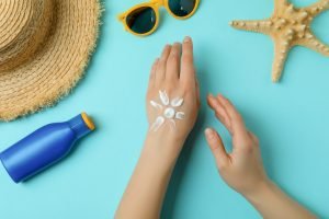 Female hands with sunscreen on blue background with summer accessories